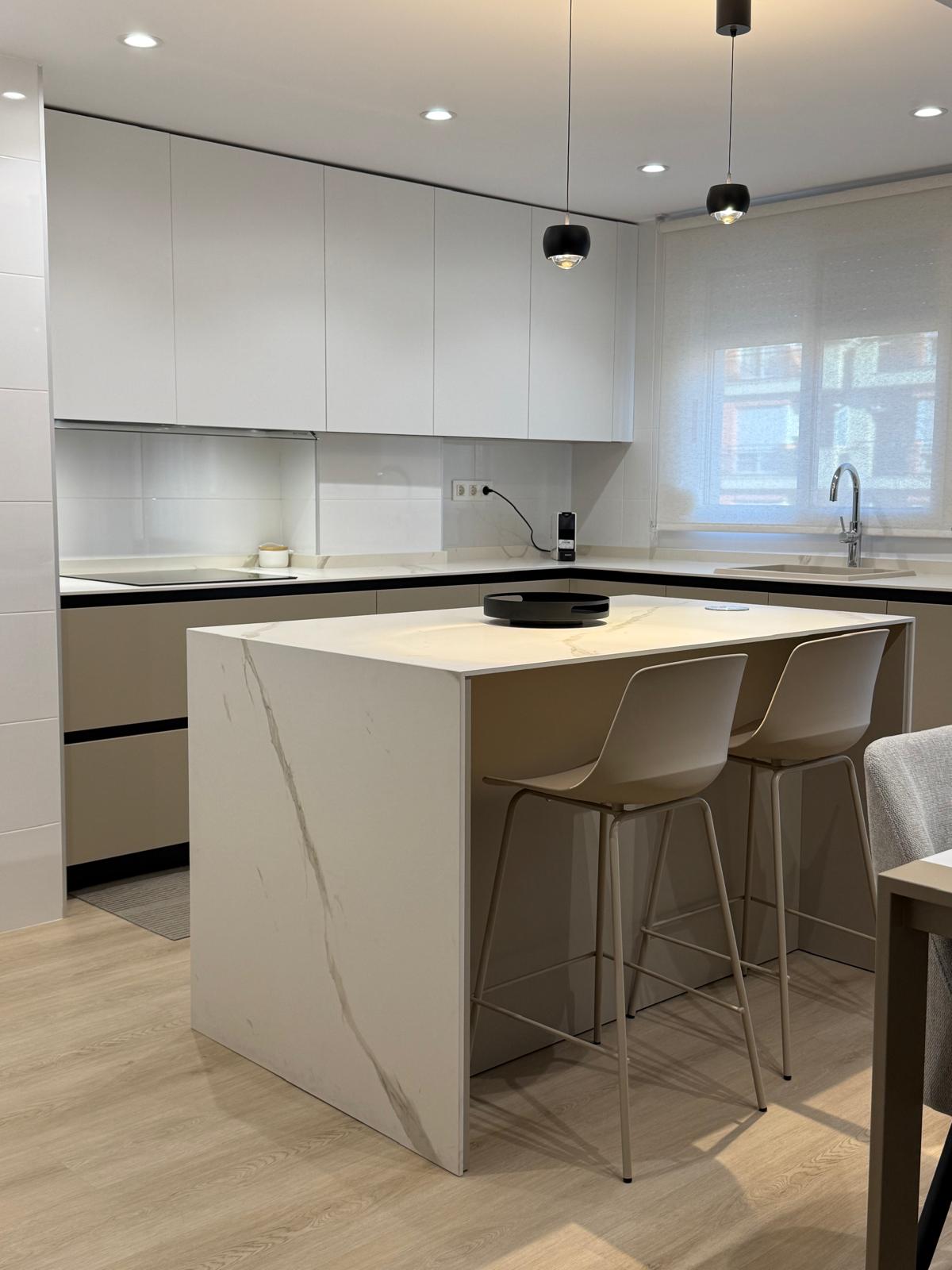 Cocina con isla central de porcelánico Laminam Calacatta Oro Venato y mueble en tono arena