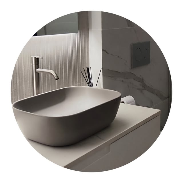 Baño con lavabo sobre encimera gris mate y pared de mármol